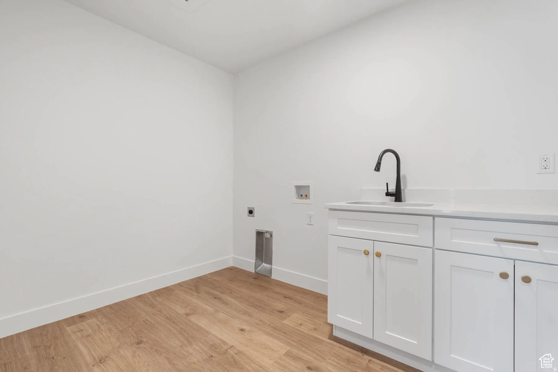 Laundry room with wood-finish flooring and a built-in white cabinetry vanity featuring a sink and matte black faucet