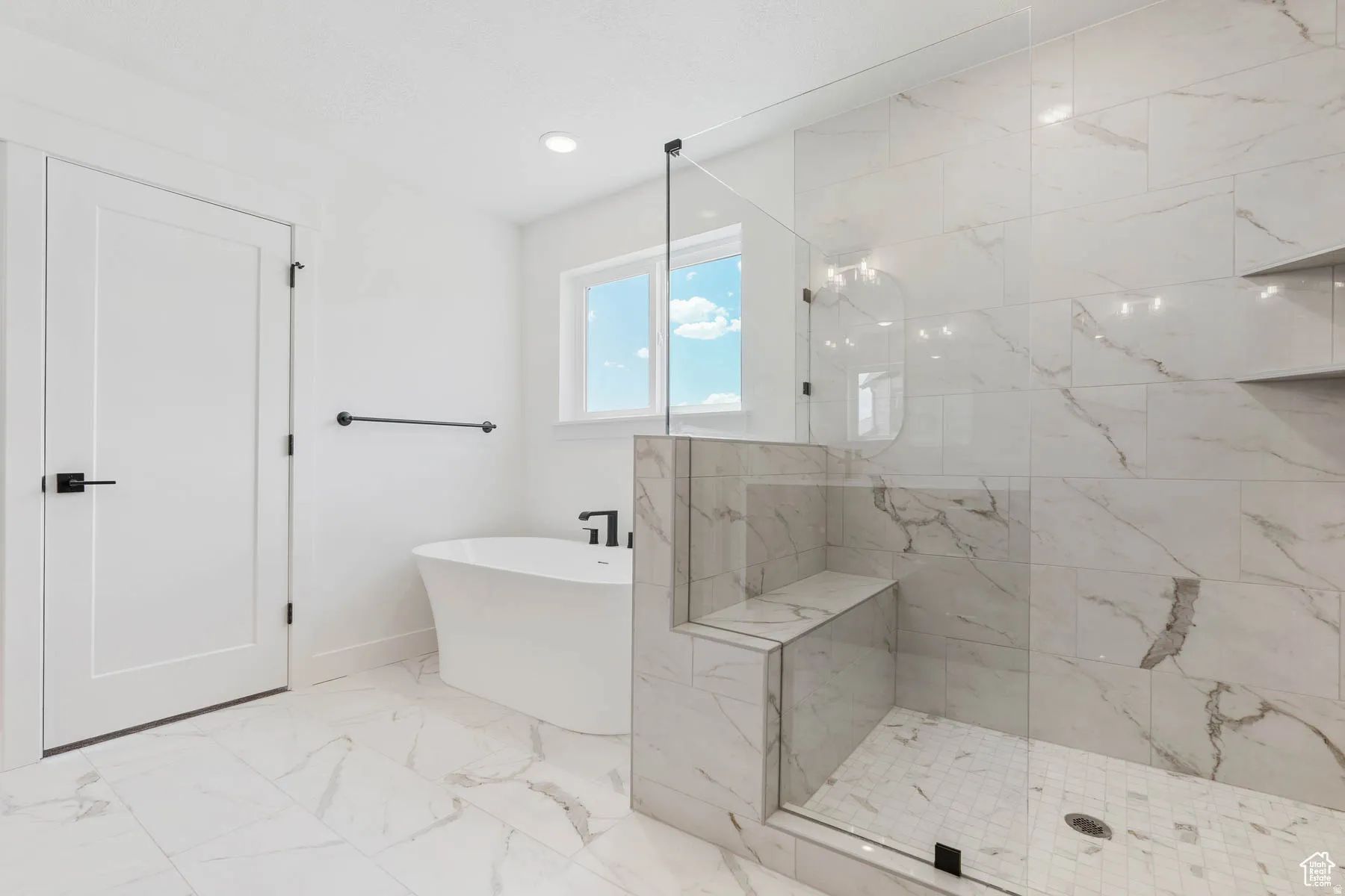 Modern bathroom featuring a freestanding soaking tub, a spacious glass-enclosed shower with integrated bench seating, and full-height marble-look tile