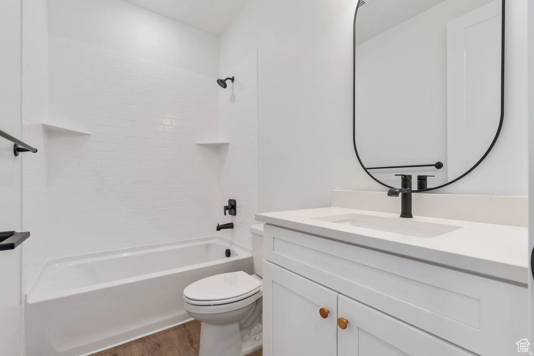 Bathroom featuring a white subway tile surround bathtub, white vanity with integrated sink, matte black fixtures, and wood-finish flooring