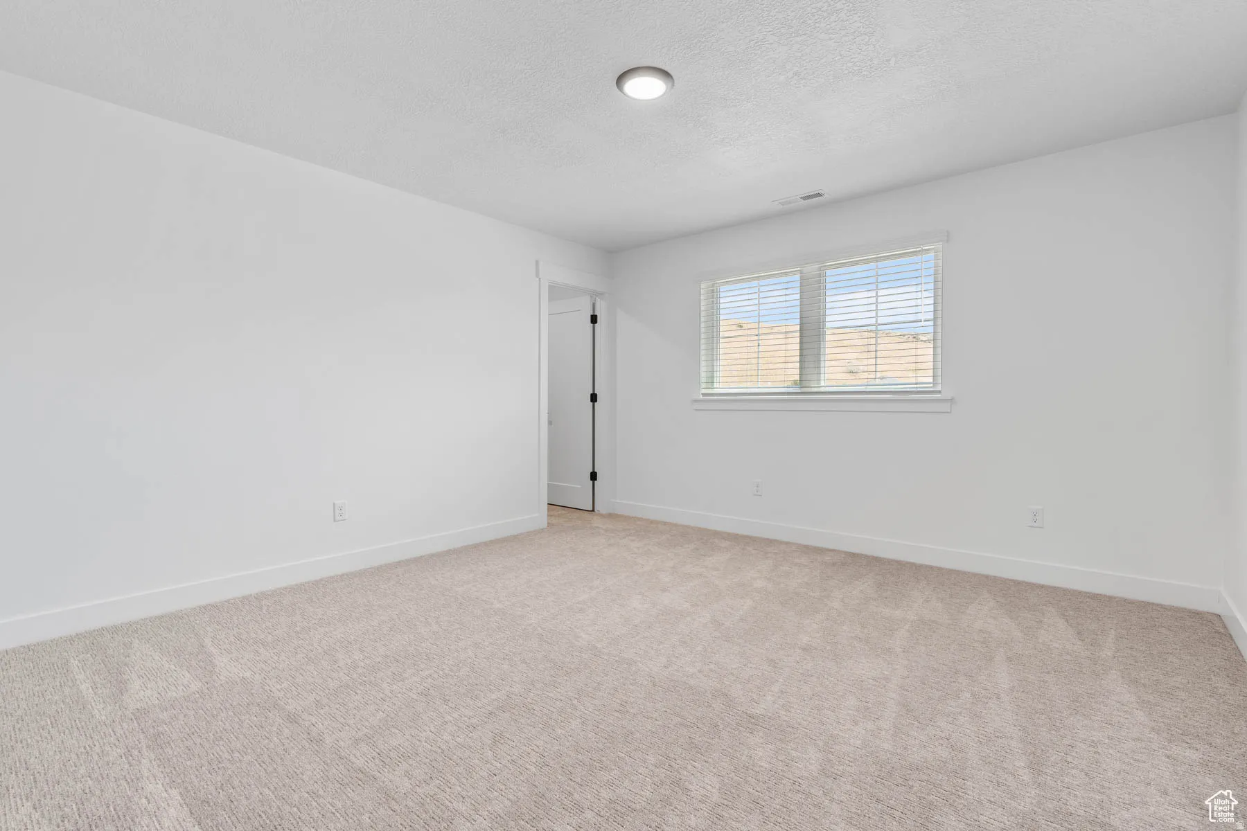 Bright room featuring light-colored carpet flooring, white walls, and a window with blinds