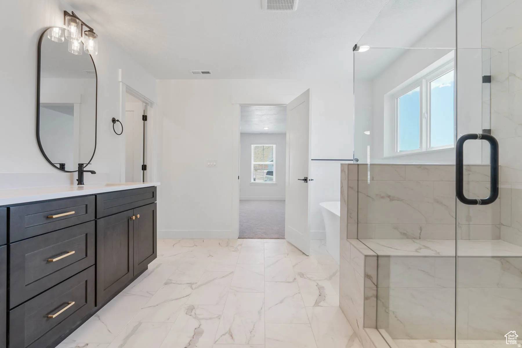 Spacious bathroom featuring a frameless glass shower enclosure with a built-in bench, a freestanding bathtub, and a double vanity with dark cabinetry and gold-tone hardware