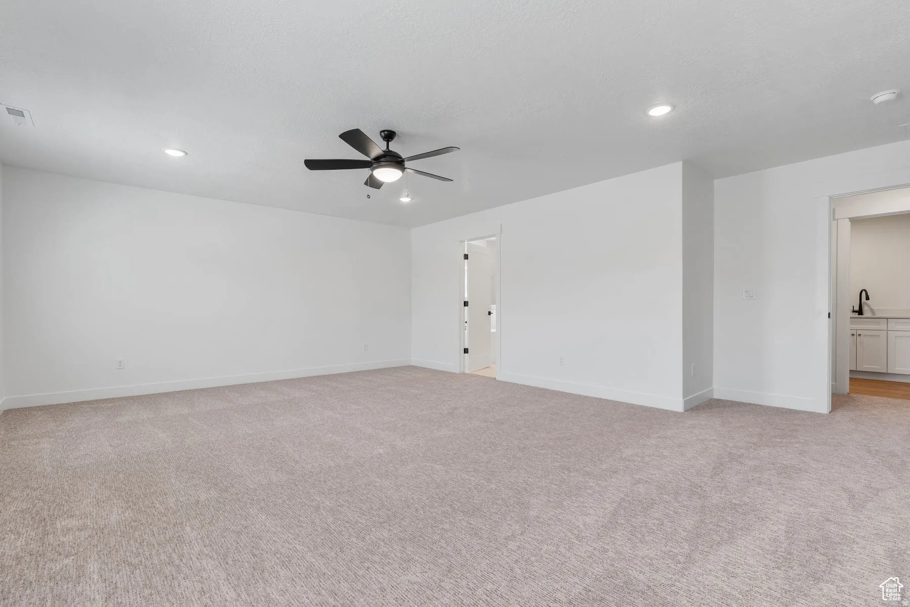 Spacious room featuring neutral carpeting, white walls, and a contemporary ceiling fan