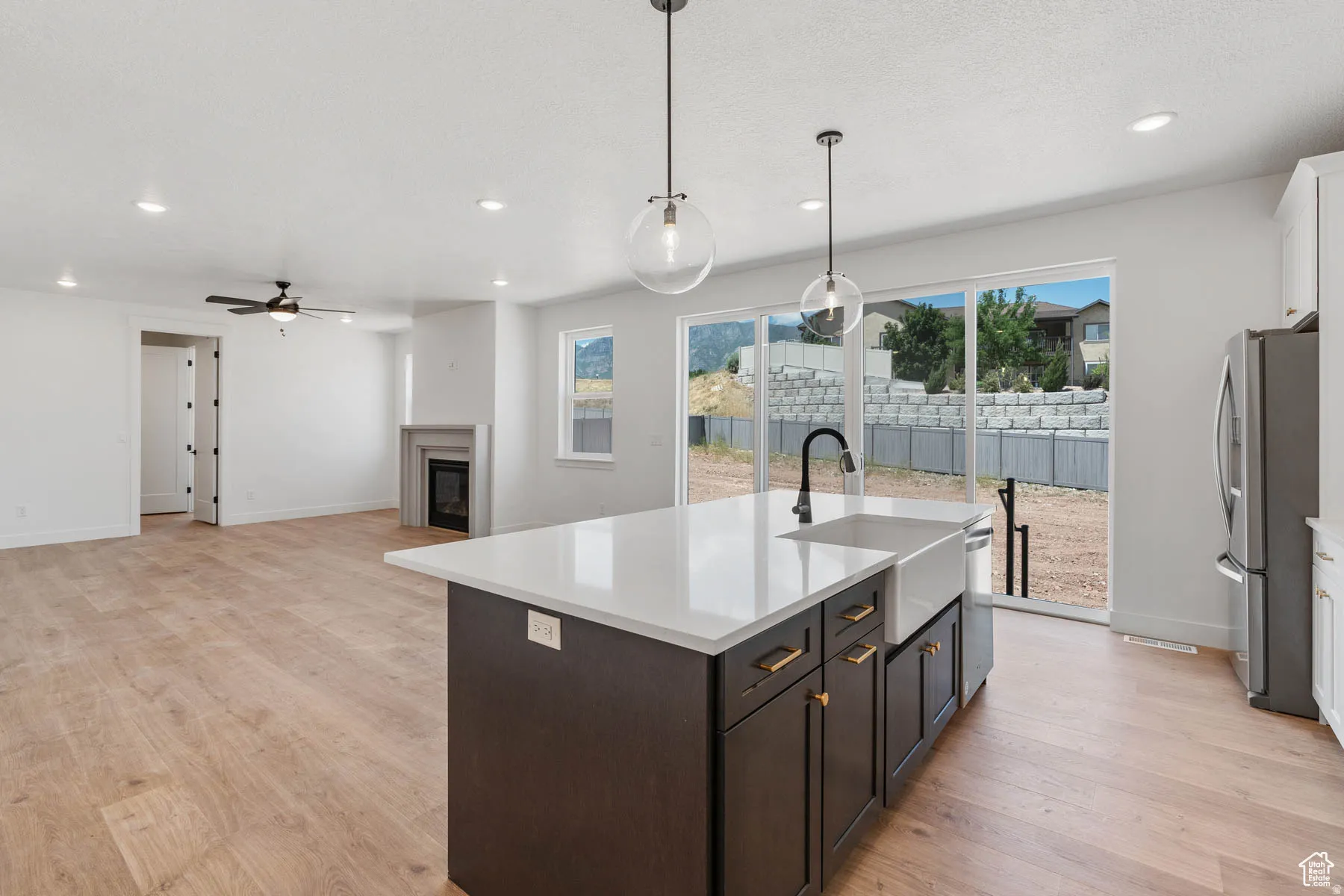 Open-concept living space featuring a central island with a farmhouse sink, stainless steel appliances, wood-finish flooring, and a fireplace with a mantel