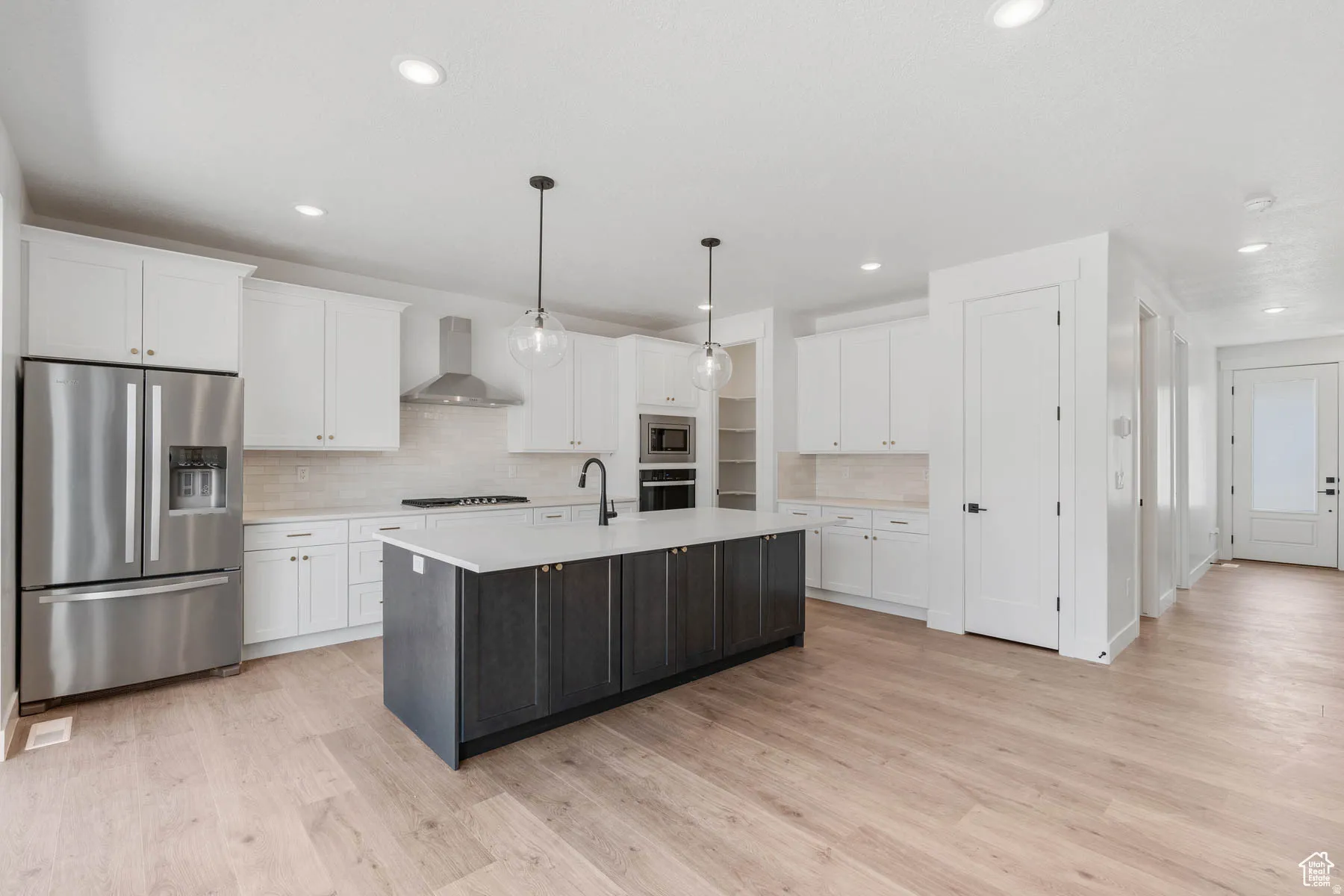 Kitchen featuring a dark-toned island with a light-toned countertop, stainless steel appliances, white cabinetry, a tile backsplash, and wood-finish flooring