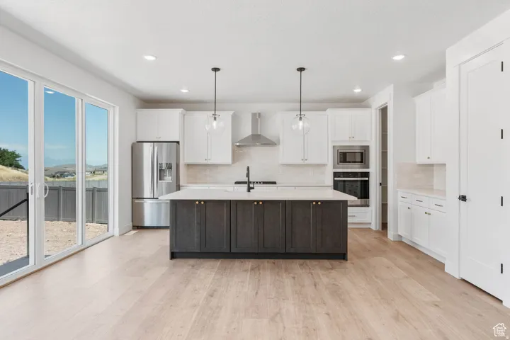 Contemporary kitchen featuring a dark-toned island with a light-toned countertop, white cabinetry, stainless steel appliances, and wood-finish flooring