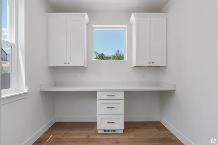 Built-in desk featuring white cabinetry with gold-tone hardware, a white countertop, and wood-finish flooring