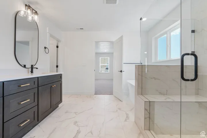 Spacious bathroom featuring a frameless glass shower enclosure with a built-in bench, a freestanding bathtub, and a double vanity with dark cabinetry and gold-tone hardware