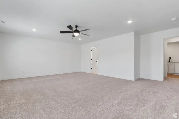 Spacious room featuring neutral carpeting, white walls, and a contemporary ceiling fan