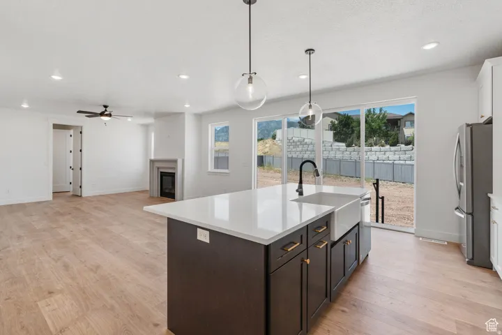 Open-concept living space featuring a central island with a farmhouse sink, stainless steel appliances, wood-finish flooring, and a fireplace with a mantel