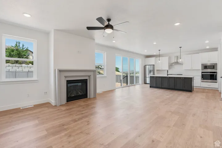 Spacious open-concept living area featuring light wood-finish flooring, a contemporary fireplace with a gray mantel, and recessed lighting
