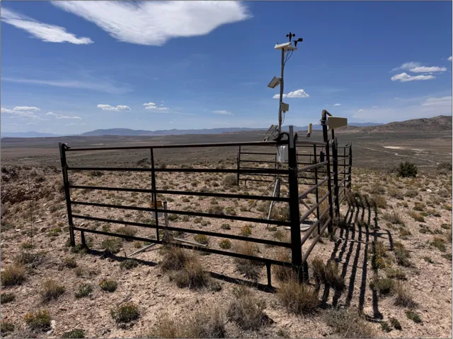 Enclosed equipment area featuring a metal fence, arid landscaping, and a distant mountainous horizon