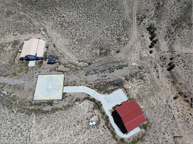 Expansive desert property featuring a helipad, a primary residence with a red roof, a secondary structure with a tan roof, concrete driveways, and solar panels