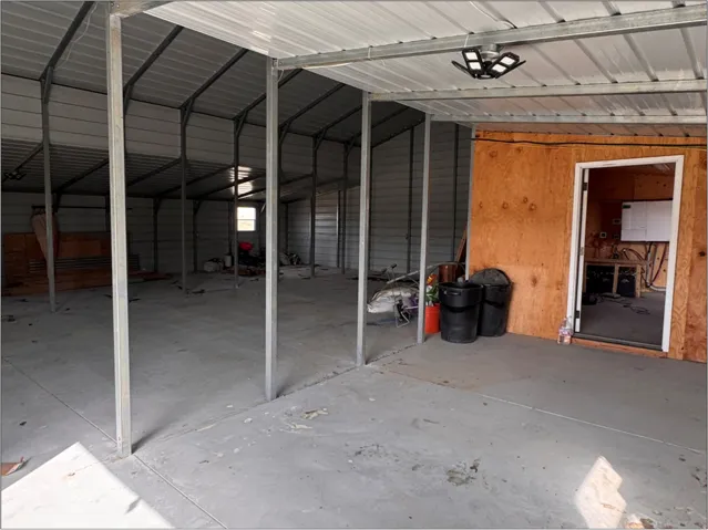 Spacious metal structure featuring a concrete slab foundation, exposed metal framing, and a separate enclosed room with a plywood exterior