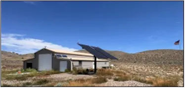 Industrial-style building featuring a light-colored metal exterior, multiple solar panel installations, and a prominent garage door