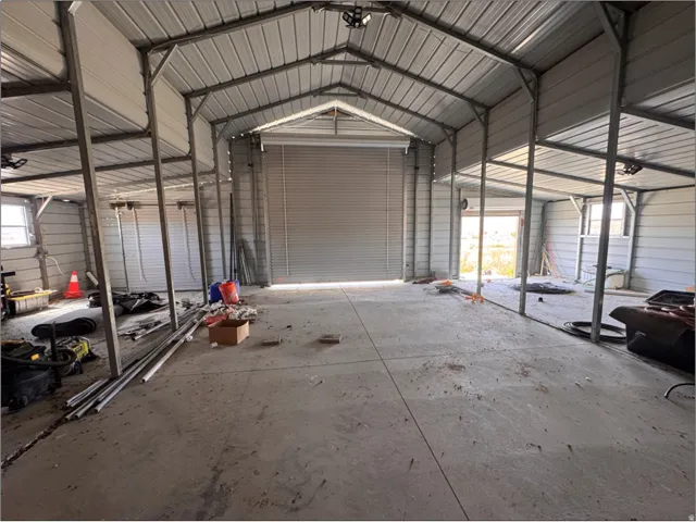 Pre-engineered metal building featuring a large roll-up door, corrugated metal siding, exposed structural steel framing, concrete flooring, and multiple windows