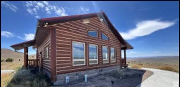 Log cabin exterior featuring a covered porch with railing, multiple windows, and a red-toned roof