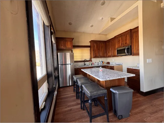 Kitchen featuring wood-finish flooring, ample wood cabinetry, light-toned countertops, a central island with bar seating, and stainless steel appliances