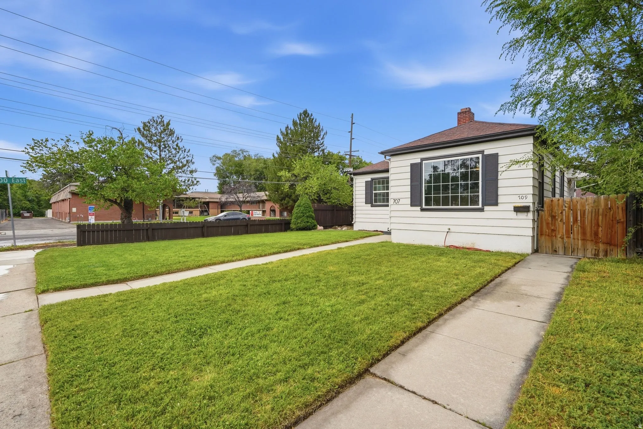 White horizontal siding exterior with dark window shutters, a front entry walkway, and a landscaped lawn