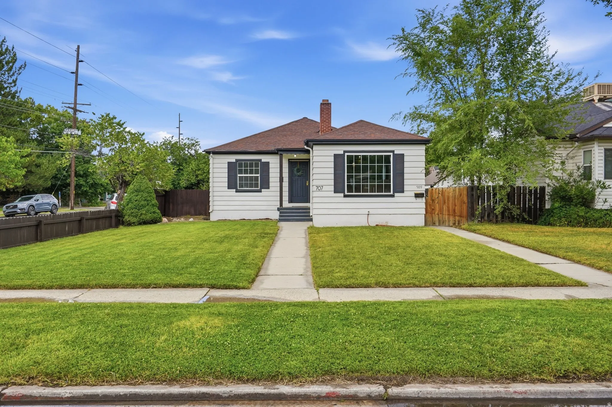White clapboard siding exterior with dark shutters, a dark front door, and an asphalt shingle roof