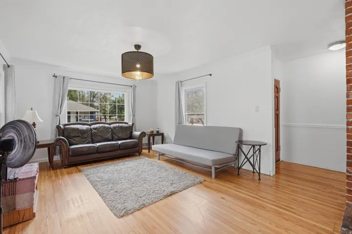 Bright living area with wood-finish flooring, white walls, and a large front-facing window