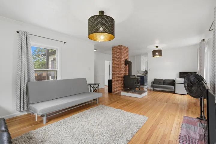 Living area showcasing wood-finish flooring, a brick fireplace surround with a black wood-burning stove, and a recessed window