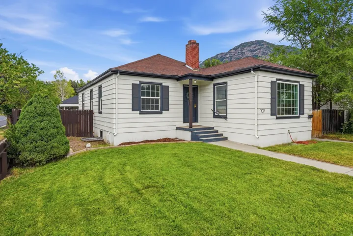 White siding exterior featuring a dark brown shingled roof, dark shutters, red brick chimney, and a landscaped front lawn