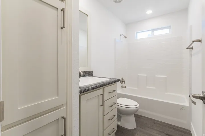 Full bathroom featuring a single vanity with a dark countertop, white undermount sink, and brushed nickel hardware