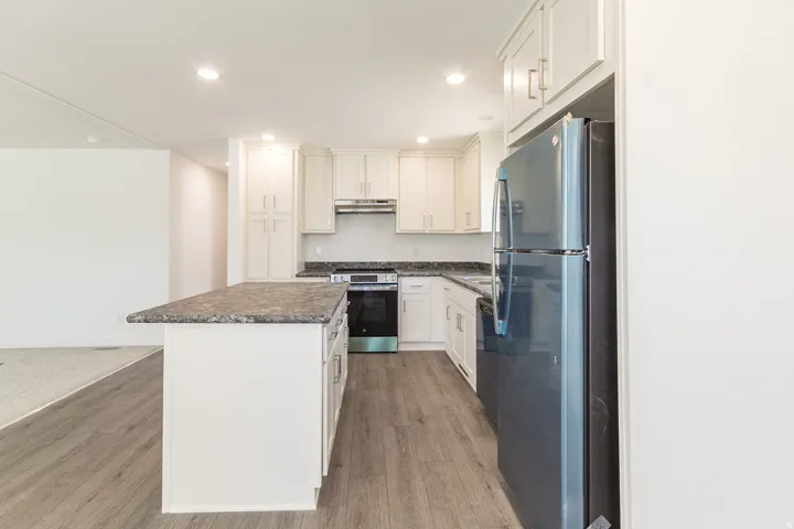 Bright kitchen featuring white cabinetry, a central island with a granite-look countertop, wood-finish flooring, recessed lighting, and a stainless steel appliance suite