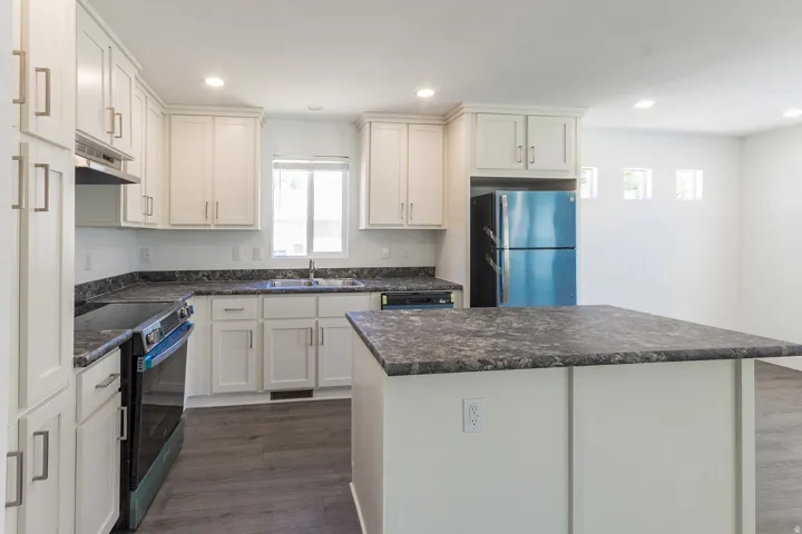 Kitchen featuring an island, white shaker-style cabinetry, dark speckled countertops, stainless steel sink with a single-handle faucet, and built-in appliances including a refrigerator and range
