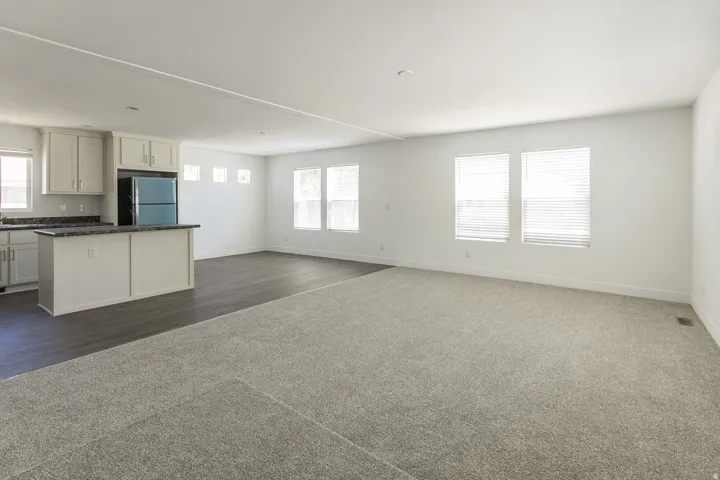 Open-concept living area featuring a kitchen island, wood-finish flooring, light-toned carpeting, white cabinetry, and multiple windows with blinds