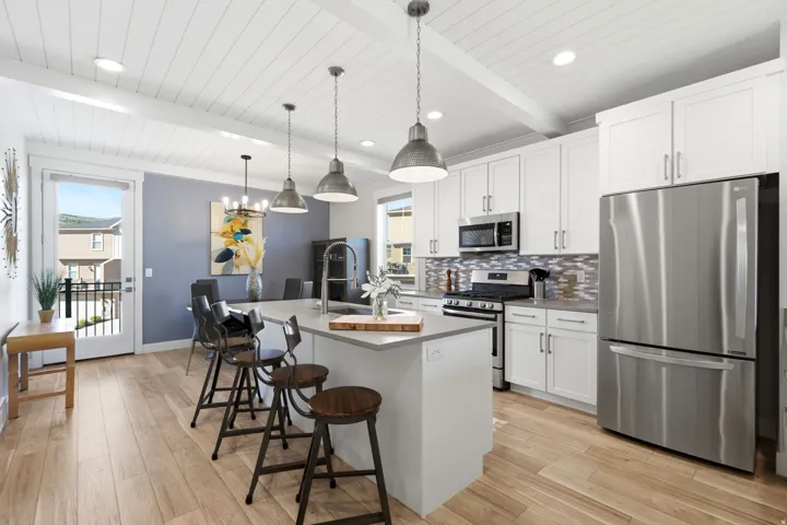 Modern kitchen featuring white shaker cabinetry, stainless steel appliances, a center island with pendant lighting, wood-finish flooring, and a glass-paneled door