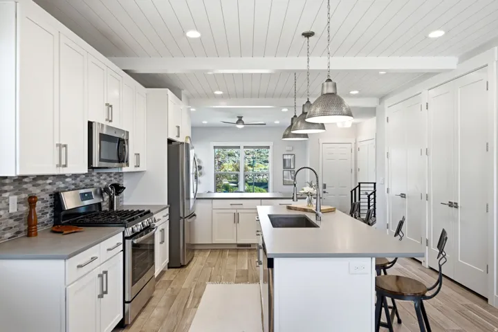 Modern kitchen featuring white shaker cabinetry, stainless steel appliances, a multi-tone tile backsplash, and a central island with an undermount sink