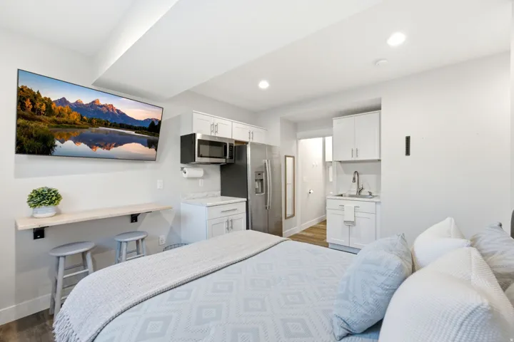 Integrated living space featuring a compact kitchen with stainless steel appliances, white cabinetry, and a light-toned countertop