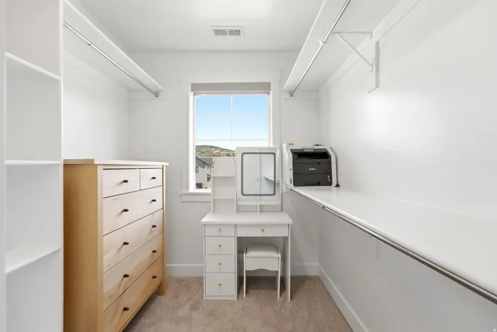 Windowed walk-in closet featuring white built-in shelving, hanging rods, and neutral carpet flooring