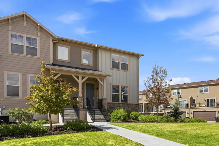 Two-story townhome with a covered entryway featuring a dark blue door and black railings