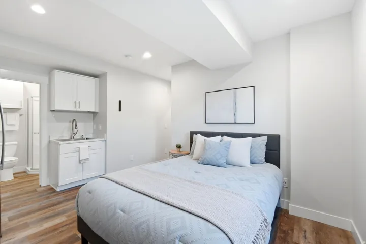 Open-concept room featuring wood-finish flooring, recessed lighting, and a kitchenette with white cabinetry and a stainless steel faucet