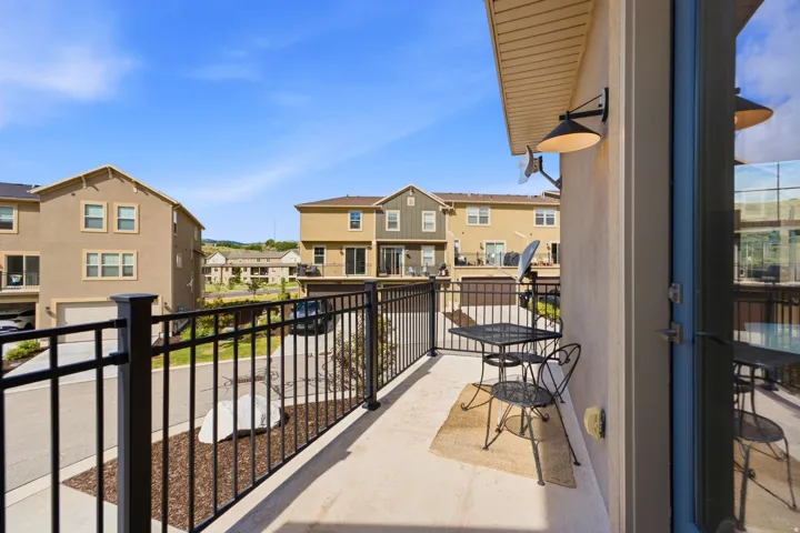 Private balcony featuring a stucco exterior, black metal railings, and an exterior wall sconce