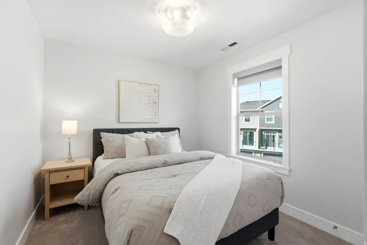Carpeted bedroom featuring a large window with white trim, a flush-mount ceiling light fixture, and neutral wall tones