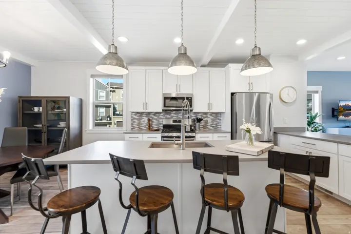 Spacious kitchen featuring an expansive island with seating, white shaker-style cabinetry, stainless steel appliances, a mosaic tile backsplash, and wood-finish flooring
