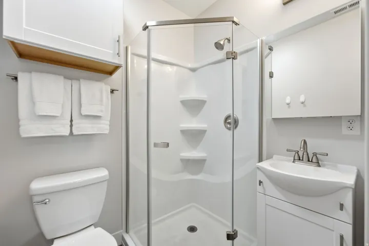 Corner glass-enclosed shower with integrated shelving, brushed nickel fixtures, and a white basin sink with coordinating vanity