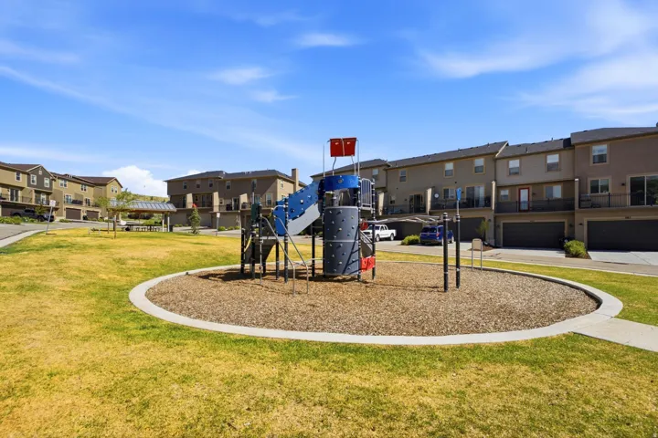 Central playground with a wood chip base, surrounded by a grassy lawn and a concrete border