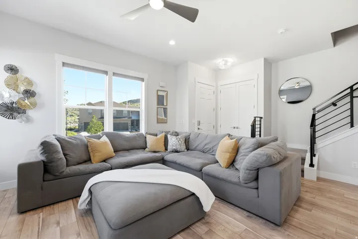 Bright living area featuring large windows, wood-finish flooring, a contemporary ceiling fan, recessed lighting, and a modern staircase with black railings