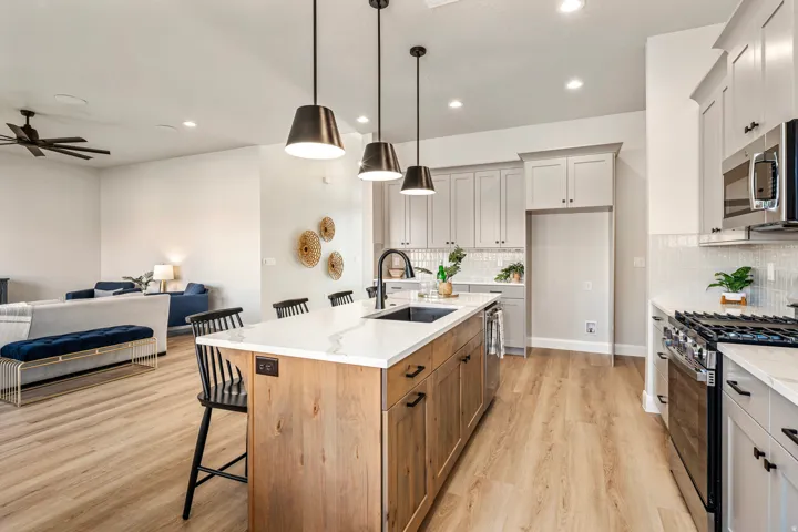 Open-concept kitchen featuring a wood-finish island with a built-in sink, white countertops, and three pendant lights