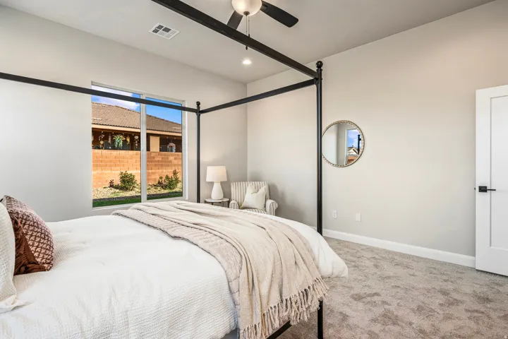 Carpeted bedroom featuring a large window, a ceiling fan, light-toned walls, a white interior door with matte black hardware, and crisp white baseboards