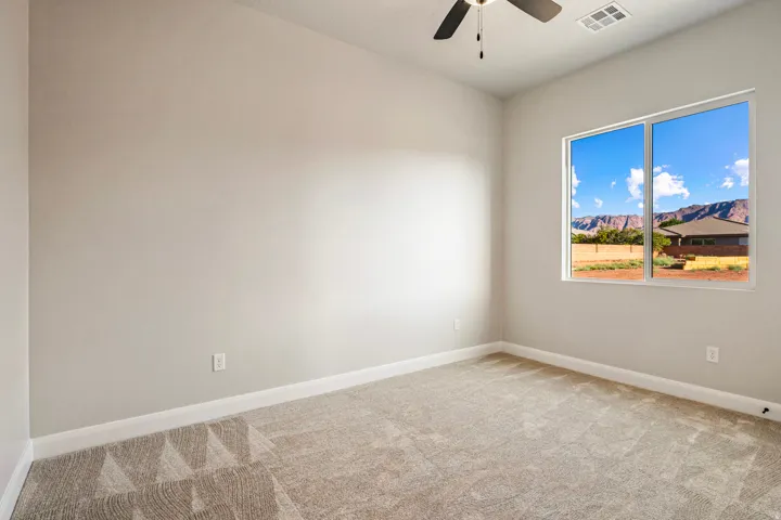 Bright room featuring a large window, neutral carpeting, a ceiling fan, light gray walls, and white baseboards