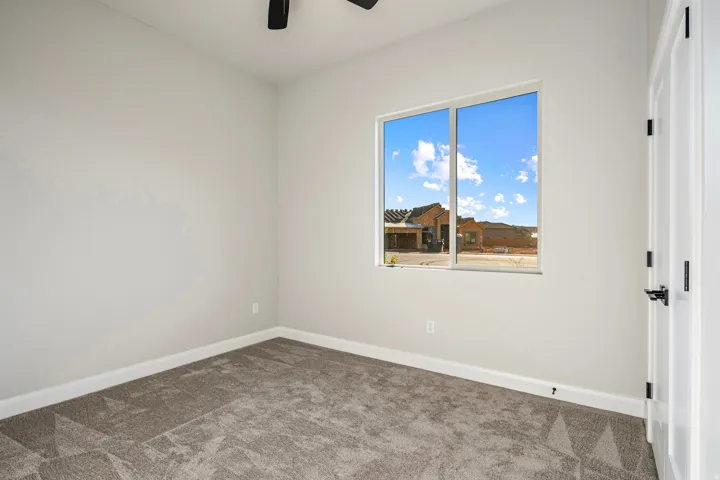 Neutral wall paint with white trim, gray patterned carpet, a ceiling fan with black blades, white interior door with black hardware, and a double-pane window