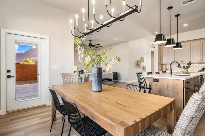 Open-concept living space featuring wood-finish flooring, a contemporary linear chandelier, an expansive kitchen island with pendant lighting, light-toned cabinetry, and a full-light rear door