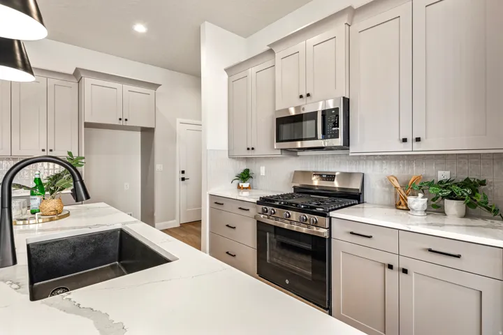 Contemporary kitchen featuring light gray cabinetry, stainless steel appliances, a black basin sink, white stone countertops, and a textured tile backsplash