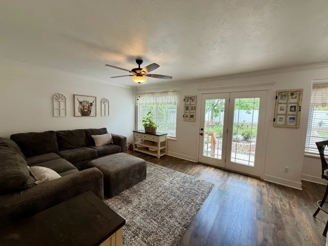 Living area featuring dark wood-finish flooring, white crown molding, and a ceiling fan with integrated lighting