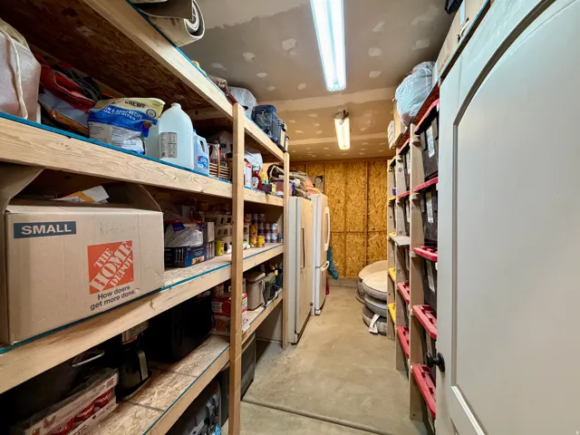Utility room featuring extensive wood shelving, a second refrigerator, fluorescent lighting, and a white interior door